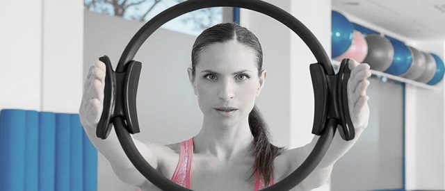 Pilates Practitioner holds up pilates circle and gazes through it at you